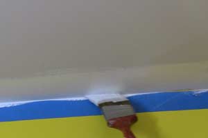 photo brushing white paint on ceiling along masking tape photo brushing white paint on ceiling along masking tape