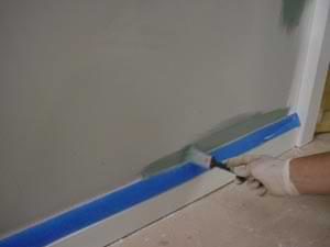 photo using a brush to paint over masking tape on a baseboard photo using a brush to paint over masking tape on a baseboard