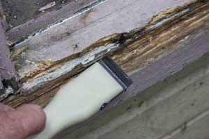 photo scraping out rotted wood on a windowsill