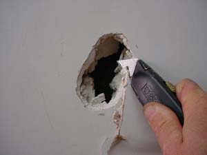 photo trimming rough drywall around a small hole